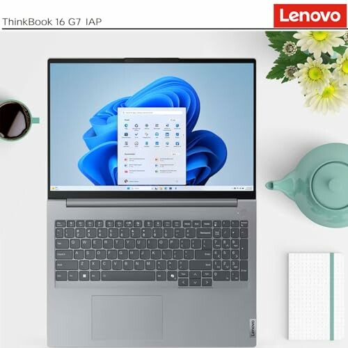 Top view of Lenovo ThinkBook 16 G7 IAP laptop with Windows interface on screen, accompanied by a teapot, cup, and flowers.