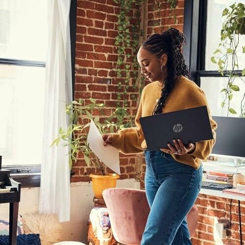 Woman holding a laptop and paper in a cozy office space.